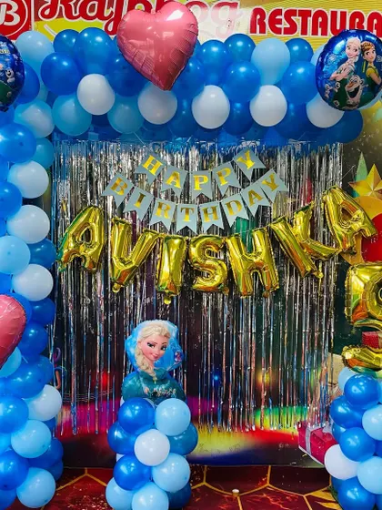A "Frozen" themed birthday party at a restaurant. The decoration includes a balloon arch with character foil balloons and a name banner over a silver foil curtain.