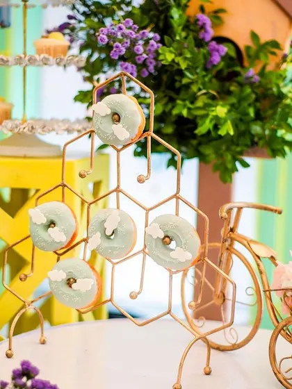 Themed donuts displayed on a gold honeycomb-style stand, with a miniature bicycle prop adding a whimsical touch.