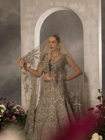 A silver-grey lehenga with a beautifully embroidered veil. The floral motifs and muted color palette make it a sophisticated choice for a modern bride.