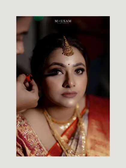 A behind-the-scenes moment of the bride getting her makeup done. Her calm expression and the artist's focused work create a sense of quiet anticipation before the main event.