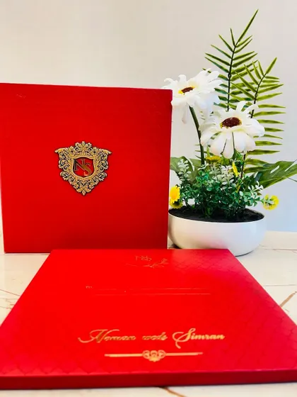 A bold and regal statement. This bright red boxed invitation features a custom metal crest with the couple's initials, set against a textured background.