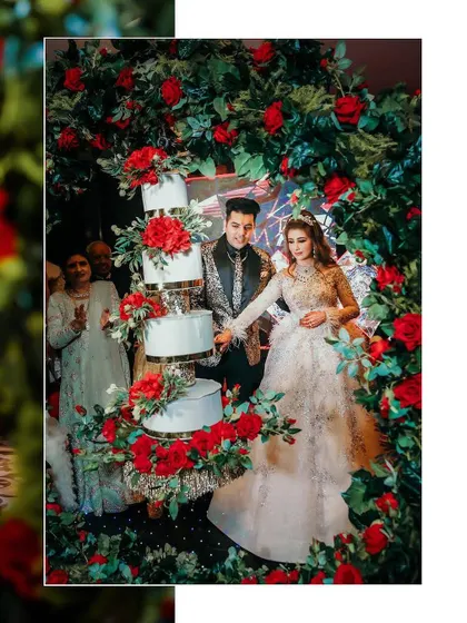 The magical moment of the cake-cutting ceremony. The couple is surrounded by a stunning arch of red roses, creating a romantic and celebratory photograph.