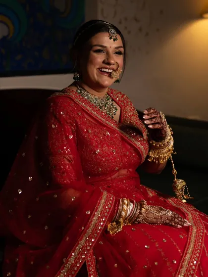 A happy, candid portrait of the bride in her red wedding attire, her smile and nose ring highlighted by the warm indoor lighting.