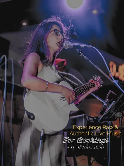 I'm playing my white guitar at the microphone in this wider view of the silver-outfit set beneath purple stage lighting.