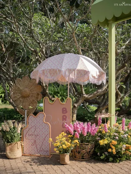 Detailed welcome signage with custom calligraphy, surrounded by flowers and a classic fringed umbrella.