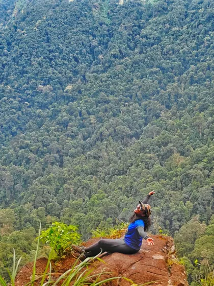 A trekker lies back on a rock, joyfully soaking in the sun and the incredible forest view.