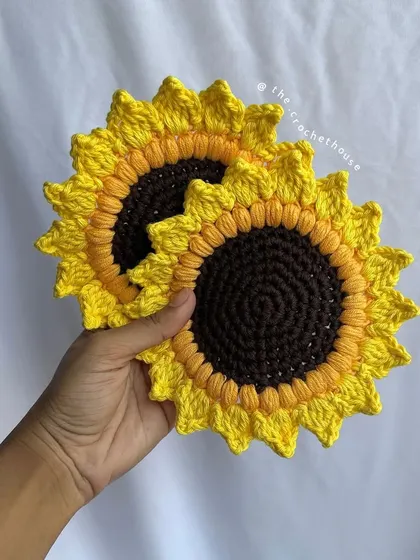 Holding up a pair of our crochet sunflower coasters. They are lightweight, durable, and made from sustainable cotton yarn.