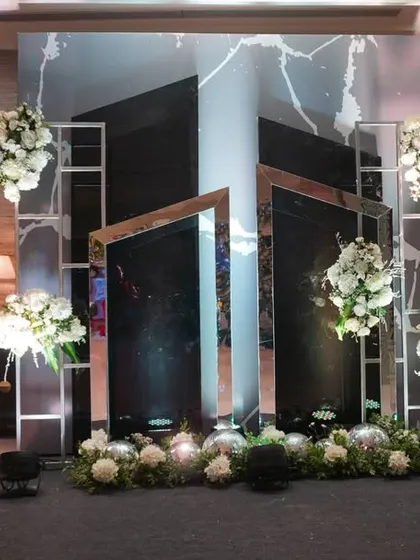 A modern and chic photo booth backdrop. The design uses angled mirrors and clean white floral arrangements to create a sophisticated and interactive space for guests to take stylish pictures.