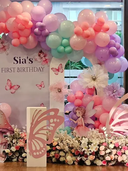 A magical fairy and butterfly theme for Sia's first birthday. The setup includes a custom backdrop, large butterfly wing props, mushroom cutouts, and a pastel balloon arch.