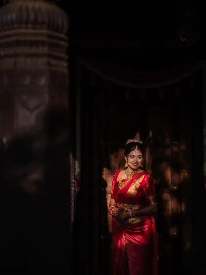 A portrait of the bride in her stunning red saree, framed by the rustic charm of her wedding venue. We focus on creating images that are both beautiful and full of character.