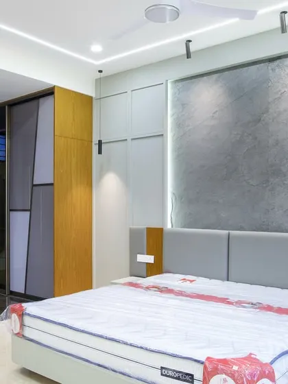 A closer view of the bedroom, highlighting the thin-cut granite slab on the wall and the custom grey paneling that conceals hidden storage. The sliding wardrobe on the left complements this with its own clean, geometric design.