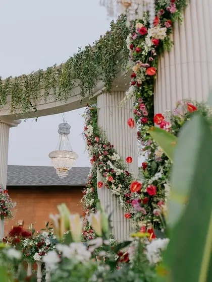 A view of the grand Roman-inspired pillar stage, seen through lush green leaves, highlighting the integration of decor and nature.