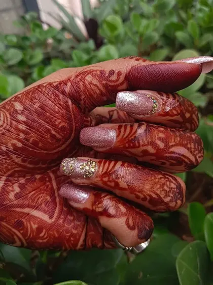 A side view showcasing the sparkle of these pink glitter and stone engagement nails against the client's intricate henna design.