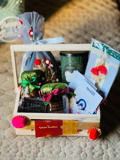 A wooden crate hamper for Rakhi, containing a scented candle, dry fruits, and a beautiful rakhi set.