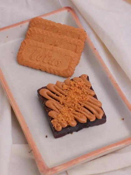 A trio of Biscoff biscuits next to our Biscoff Brownie. The crunchy, caramelized flavour of the biscuit is infused throughout the topping.