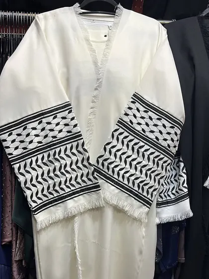A striking white abaya with black and white patterned cuffs inspired by the keffiyeh design. The frayed edges add a modern touch to this unique piece.