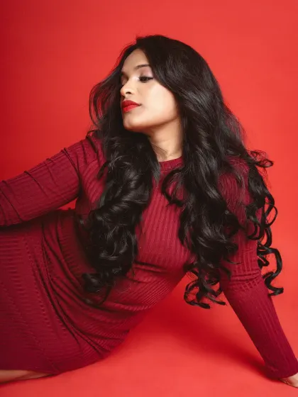 A classic portrait against a red background. The model is captured in profile, with soft lighting highlighting her features and the rich texture of her hair.