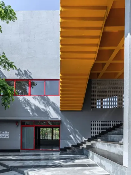 Another view of the entrance at L'Atelier, where the interplay of grey walls, a bright yellow staircase, and red window frames creates a vibrant and dynamic architectural statement.