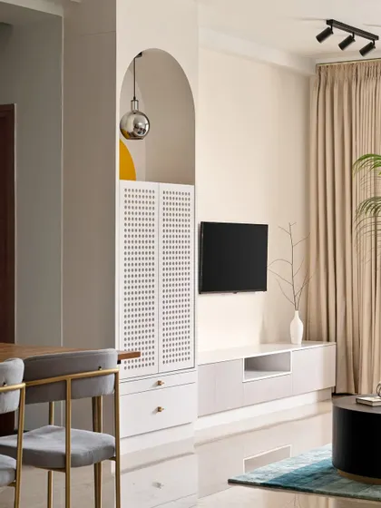 A contemporary puja cabinet is integrated into the TV unit, featuring an arched niche and perforated shutters. This design provides a dedicated spiritual corner that blends seamlessly with the modern living room aesthetic.