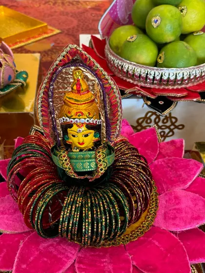 A close-up of a bangle platter for a traditional ceremony. The goddess idol sits on a pink lotus base, encircled by red and green bangles, symbolizing prosperity and happiness.