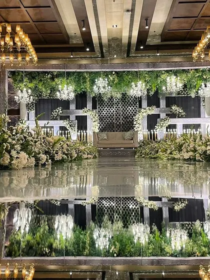 A luxury reception stage with a mirrored floor that reflects the stunning all-white floral decor and chandeliers, doubling the glamour.