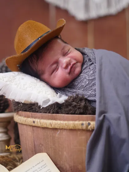 A sweet, sleepy shot of the baby in a rustic bucket prop. The natural textures of the wood and jute create a warm, earthy feel.