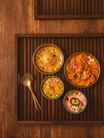 A wider flat lay of the Indian dessert spread, showing more of the wooden tray and spoons. This gives context and enhances the rustic, traditional feel of the sweets.