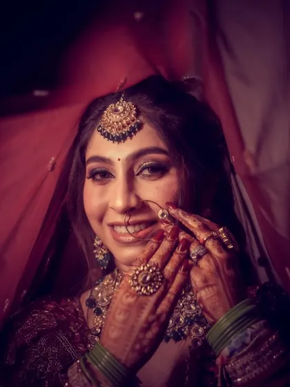 A coy and beautiful bridal portrait, with the bride partially hiding her face, drawing attention to her eyes and henna.