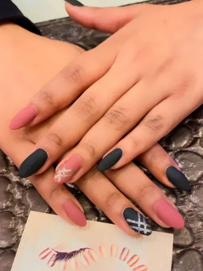 A stylish and modern set with a mix of matte black and matte pink almond nails. The design is accented with geometric and snowflake-like patterns in silver.