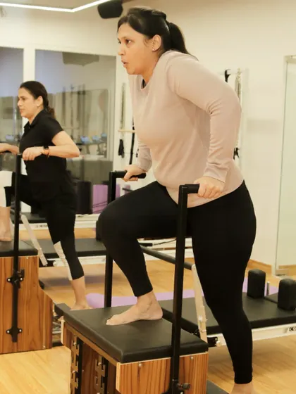 Two clients work in sync on the Pilates chair, showing the motivating atmosphere of our group classes.