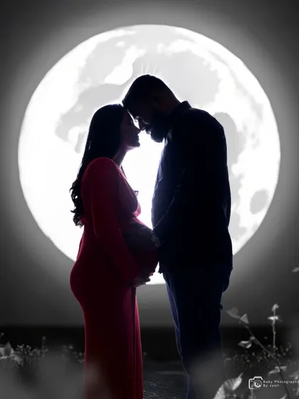 A black and white silhouette of a couple in front of the moon backdrop, creating a classic and artistic pregnancy portrait.