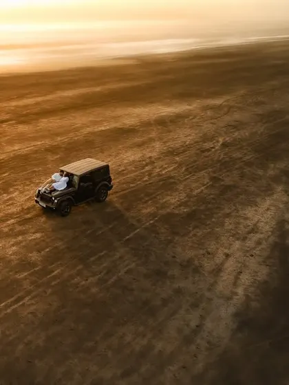 A breathtaking drone shot of a G-Wagon driving on a beach during sunset, symbolizing a journey of love and adventure.