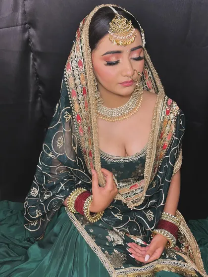 A charming bride in a deep green sharara suit. Her makeup features warm, peachy tones on the eyes and lips to create a beautiful contrast with her outfit.
