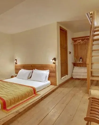 A unique room layout with a floor-level bed and a wooden staircase leading to a loft space, maximizing the use of vertical height.