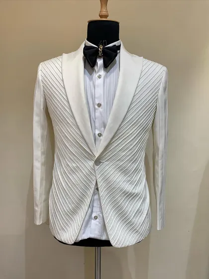 This ivory tuxedo jacket features structured, diagonal pleating across the entire garment, creating a unique texture and a sharp, architectural look. It's a subtle yet highly detailed option for a sophisticated event.