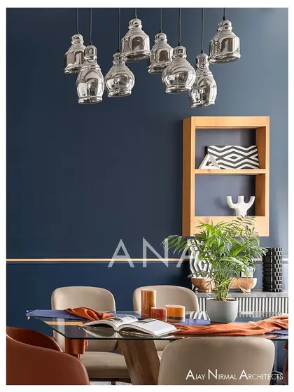 A close-up of the dining area in Apartment 704, highlighting the cluster of hanging lights and the wooden shelf. These elements add a touch of modern design against the bold blue wall.