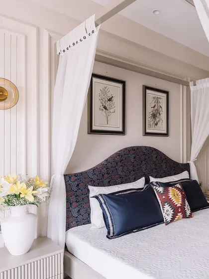 A view of the custom-upholstered headboard with a dark floral pattern, set against a wall with elegant molding and framed botanical art, blending classic and modern styles.