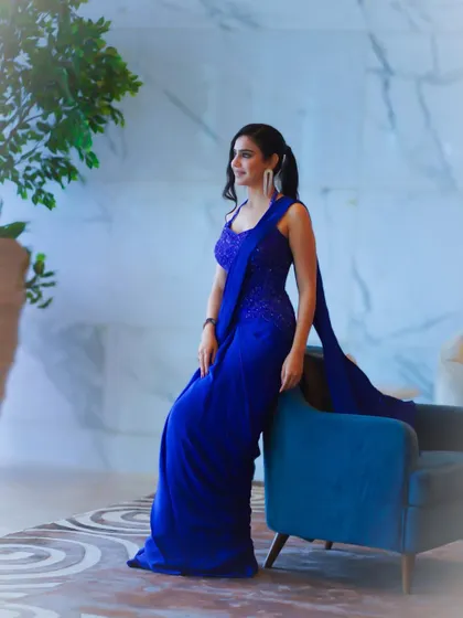 A full-length pose against a blue chair, demonstrating how to style a monochromatic look with elegance.