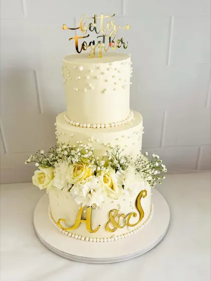 A classic and timeless three-tier wedding cake. The simple pearl detailing and arrangement of fresh baby's breath and yellow roses create a look of pure elegance.