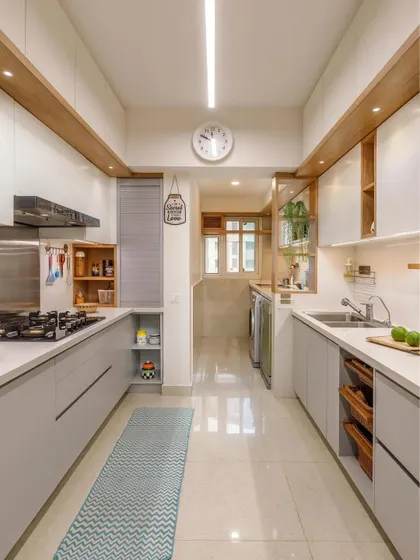 A long, parallel kitchen layout that seamlessly integrates a utility area. The design uses light grey cabinets and wood accents to create a sense of spaciousness.