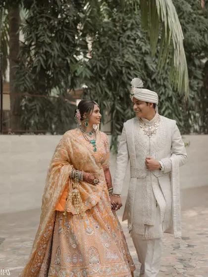 A lovely shot of the couple walking together, showcasing the bride's beautiful peach lehenga and the groom's elegant white sherwani.
