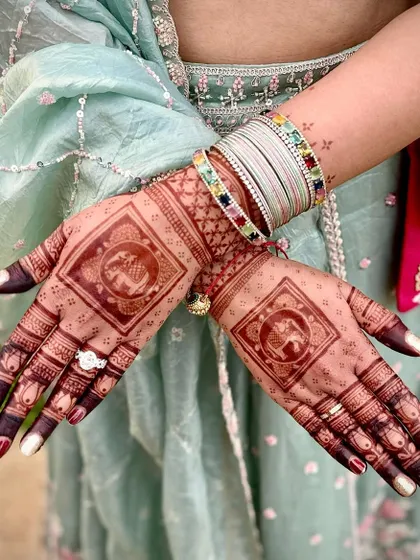 This design features a central square element with a traditional elephant motif, a symbol of good luck and prosperity. The fingers are tipped with dark henna for a classic bridal look.