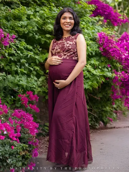 The vibrant pink of the bougainvillea flowers provides a stunning natural backdrop for this maternity portrait.