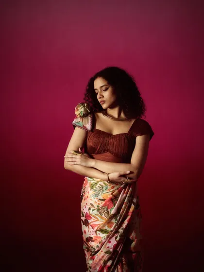 This look features natural curls and soft, earthy makeup tones that complement the printed saree and fringed blouse, creating a cohesive, bohemian-inspired fashion look.