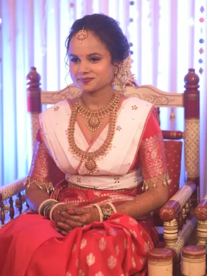 This bride is ready for her ceremony, dressed in a traditional red and white saree. The makeup is classic, with a focus on defined eyes and a matching bindi.