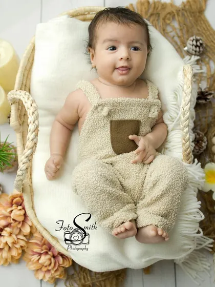 A cozy and rustic newborn setup. The soft, textured overalls and the warm, earthy tones of the props create a feeling of comfort and security.