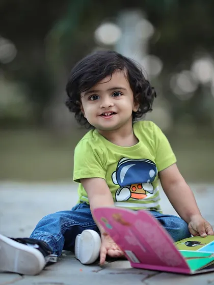 A candid moment of a toddler sitting on the ground outdoors with a book. This photo captures a quiet, thoughtful side of childhood.