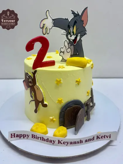 A playful Tom and Jerry cake for a 2nd birthday. The design shows Tom and Jerry in a classic chase scene, complete with edible cheese and a mouse hole, all on a yellow whipped cream cake.