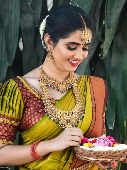 This bride looks absolutely radiant holding a basket of fresh flowers. Her glowing skin and bright smile are the centerpieces of this traditional South Indian look.