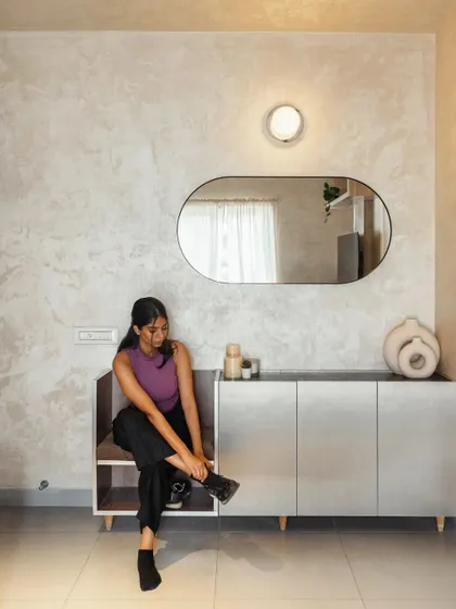 The entryway features a custom-designed console with an integrated seat for putting on shoes. This small but thoughtful detail adds functionality to the space, keeping it organized and welcoming. The textured wall finish and organic-shaped mirror add a touch of warmth and style.